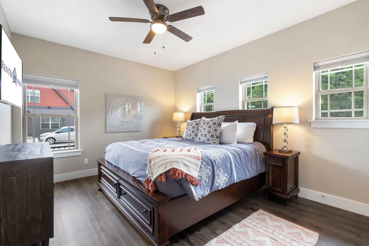 A king-sized bed with cozy bedding, nightstands with lamps, and decorative artwork create an inviting, peaceful atmosphere. Natural light filters in through the window, enhancing the tranquil mood and showcasing features ideal for a restful bedroom retreat.