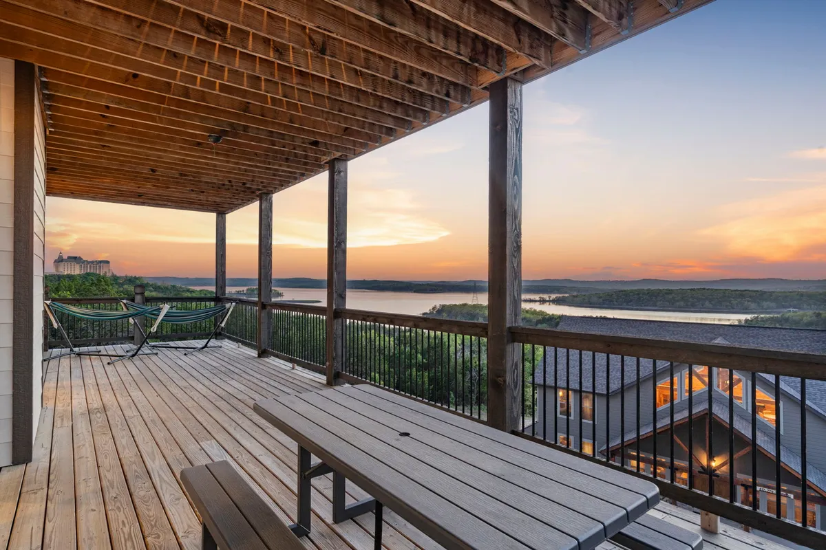 A tranquil deck scene featuring a hammock, outdoor dining table, and a spectacular sunset casting warm colors across the lake and horizon. The inviting setup encourages relaxation and gatherings with friends or family.