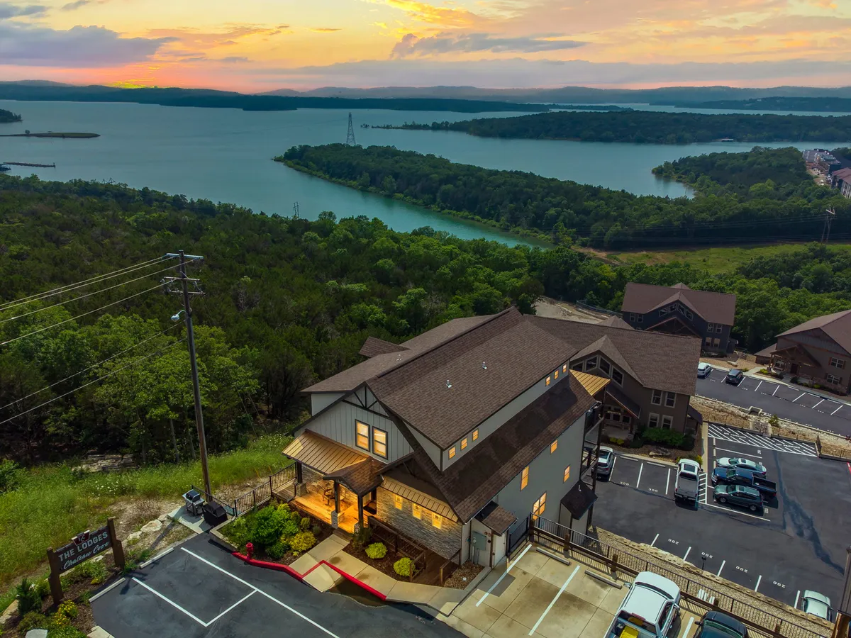 An inviting exterior shot featuring the lodge building nestled beside the lake, embraced by greenery and illuminated by a glowing sunset sky. The scene captures the all-season appeal of the property and its proximity to nature.