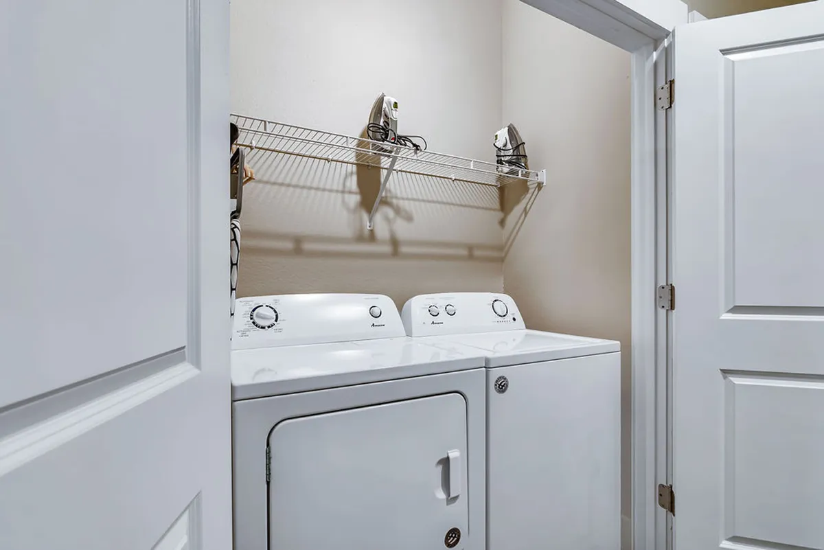 A functional laundry room with a washer, dryer, and organized shelving unit. The clean, modern design conveys efficiency and ease of use—perfect for extended stays and families needing multiple laundry facilities.
