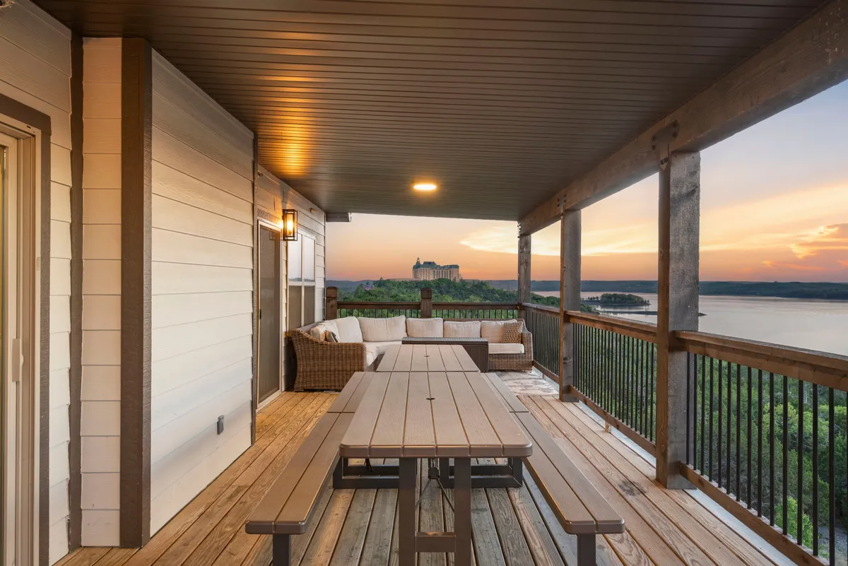 A serene exterior view of a deck featuring dining and sofa seating, all oriented towards a breathtaking lake and sunset panorama. The setup encourages relaxation and social interaction, ideal for group gatherings at any time of day.