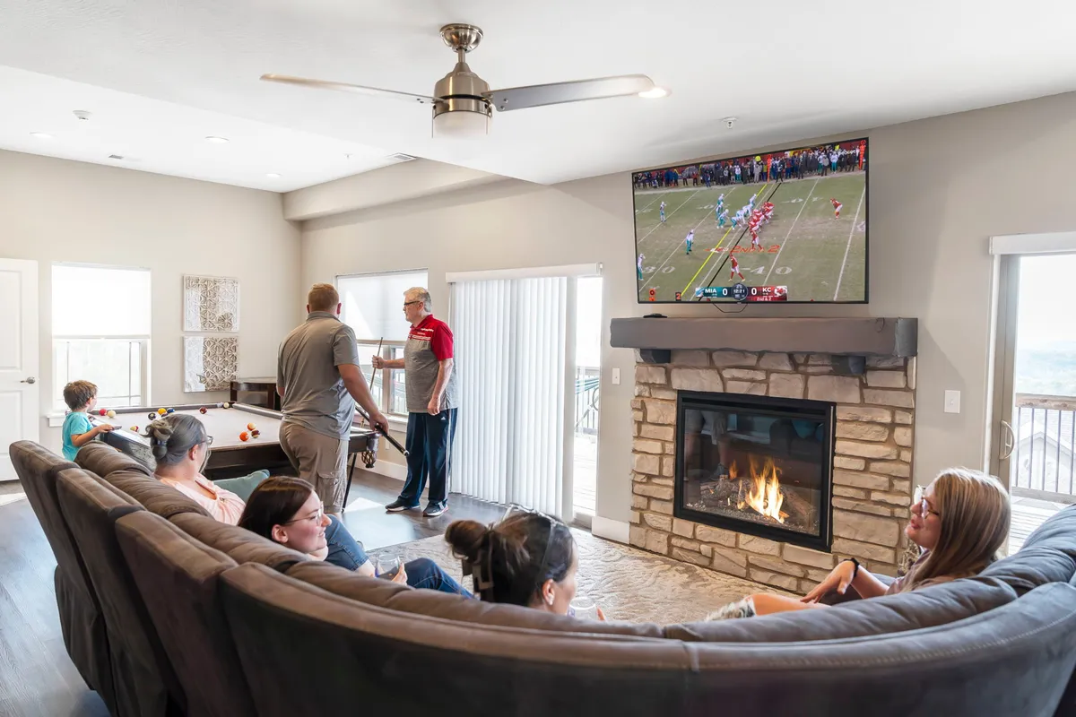 This inviting interior showcases a large sectional sofa facing a fireplace and television, with a pool table positioned in the open, bright living space. The mood is cheerful and relaxed, supporting group gatherings and multiple activities.