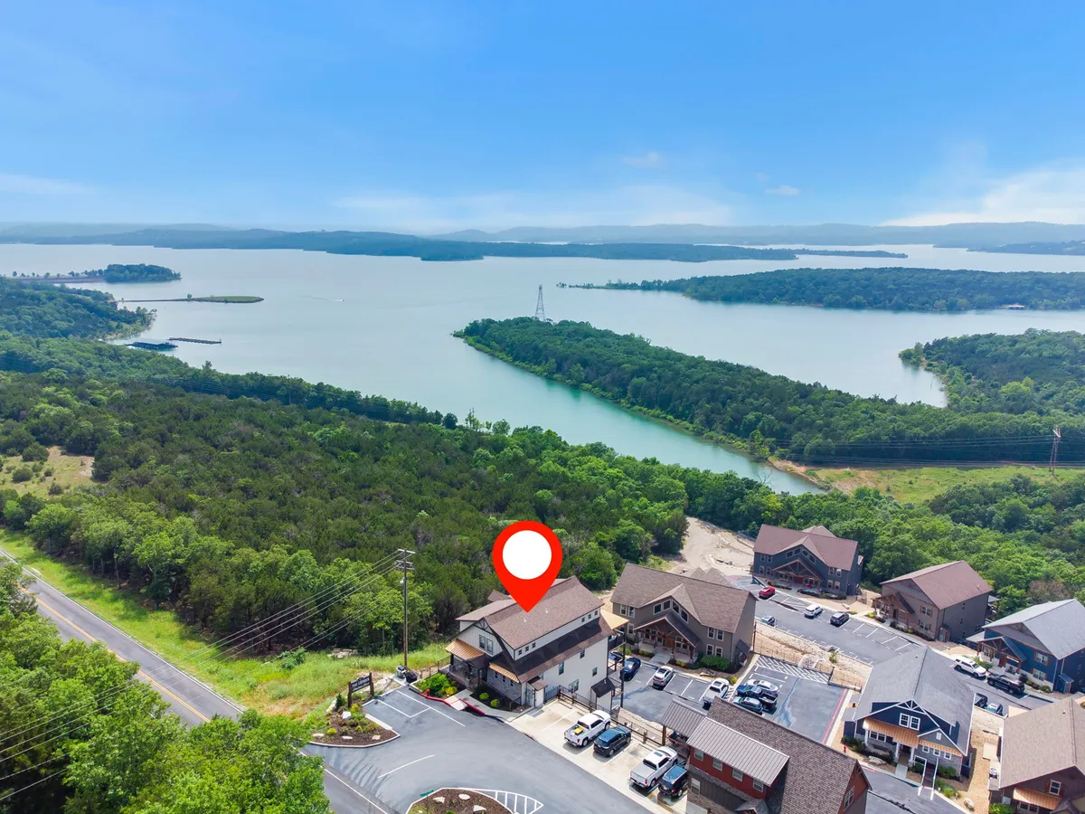 A serene exterior view of Table Rock Lake with lush greenery surrounding the shoreline, a visible road and parking area in the foreground, and expansive water extending toward the horizon. The scene evokes outdoor adventure and lakeside relaxation.