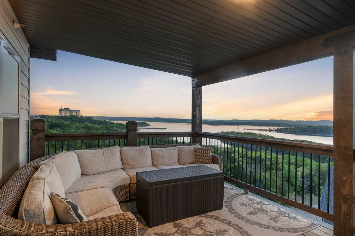 An inviting outdoor sectional sofa and coffee table arranged to overlook a stunning sunset view over the lake. The space is set up for relaxation and social gatherings, with the surrounding landscape enhancing the tranquil atmosphere.
