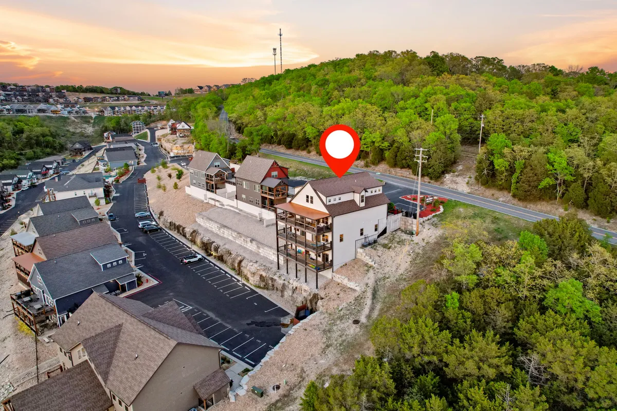 A wide exterior shot of the house showcasing its modern design, surrounded by lush green landscape and set beneath a colorful sunset sky. The spacious deck is visible, hinting at outdoor gathering spaces ideal for large groups to enjoy together.