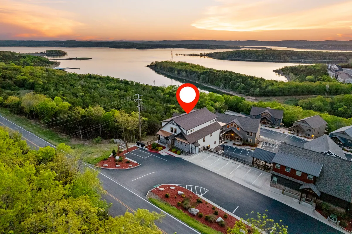 This exterior image shows the main property building set against a backdrop of Table Rock Lake, abundant greenery, and a glowing sunset sky. The scene conveys proximity to the water and the natural beauty surrounding Chateau Cove, inviting viewers to imagine outdoor activities.
