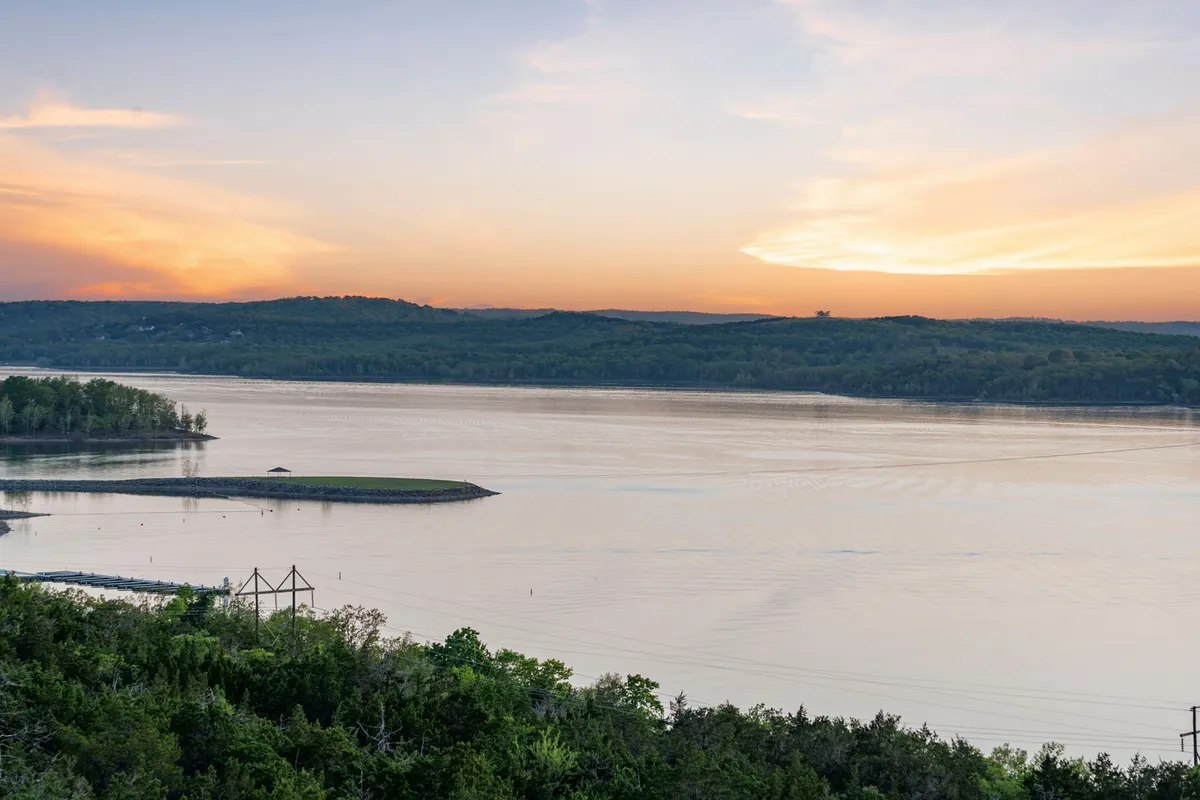 A scenic exterior view of a calm lake at sunset, with distant hills in the background and tranquil water in the foreground. The serene mood invites thoughts of lakeside relaxation, boating, and enjoying nature.