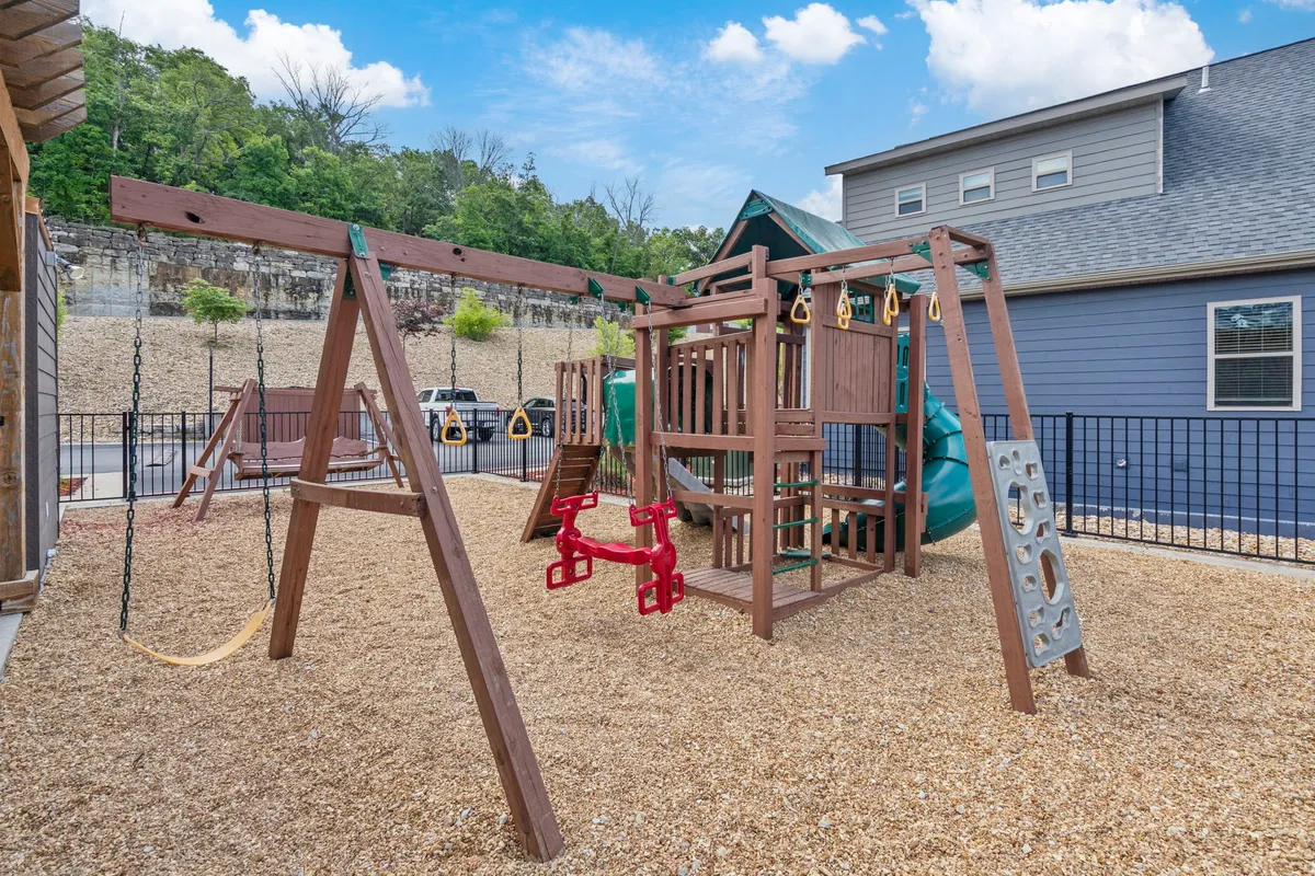 An exterior shot of a colorful playground structure with swings, a slide, and a sand area. Children are seen playing, and the surrounding area is designed for safe, joyful family gatherings.
