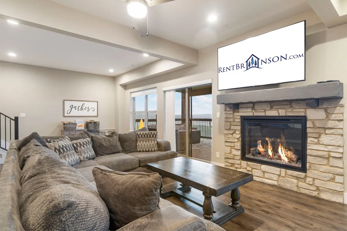 A spacious, open living area featuring a large sectional sofa, a cozy fireplace, a TV, and a wooden coffee table. The room is designed for gatherings, relaxation, and entertainment, with an inviting layout perfect for large groups.