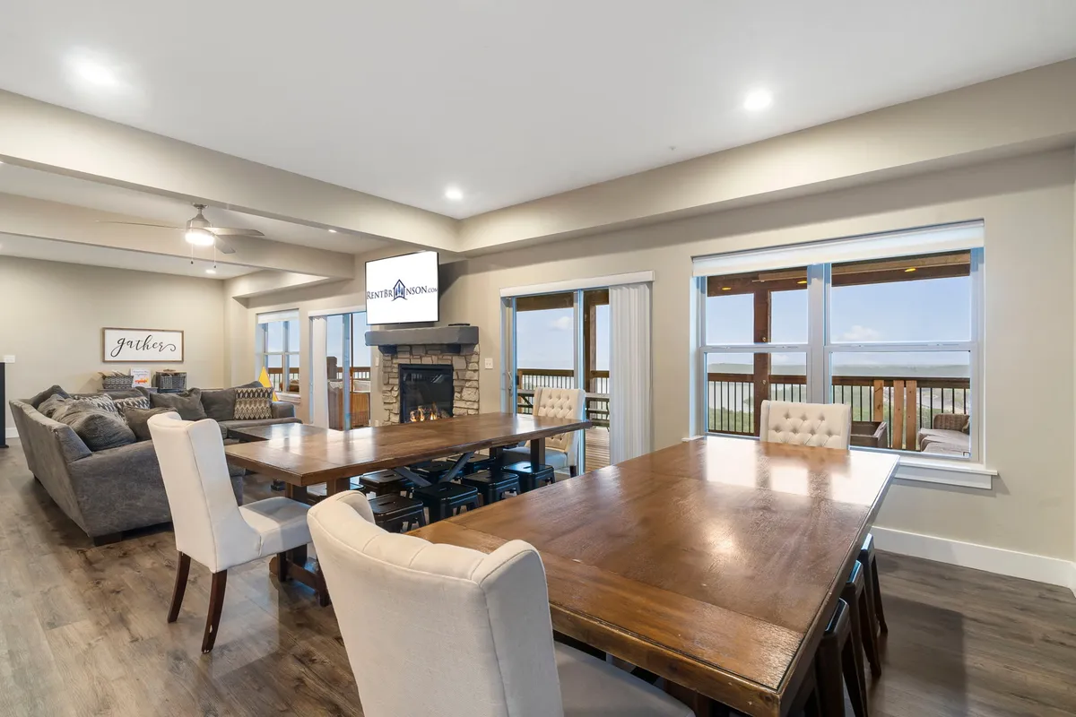 A bright and inviting dining area with a large dining table set near a fireplace and a comfortable seating area. Ample windows showcase views, and the overall space is designed for large groups to dine and converse together.